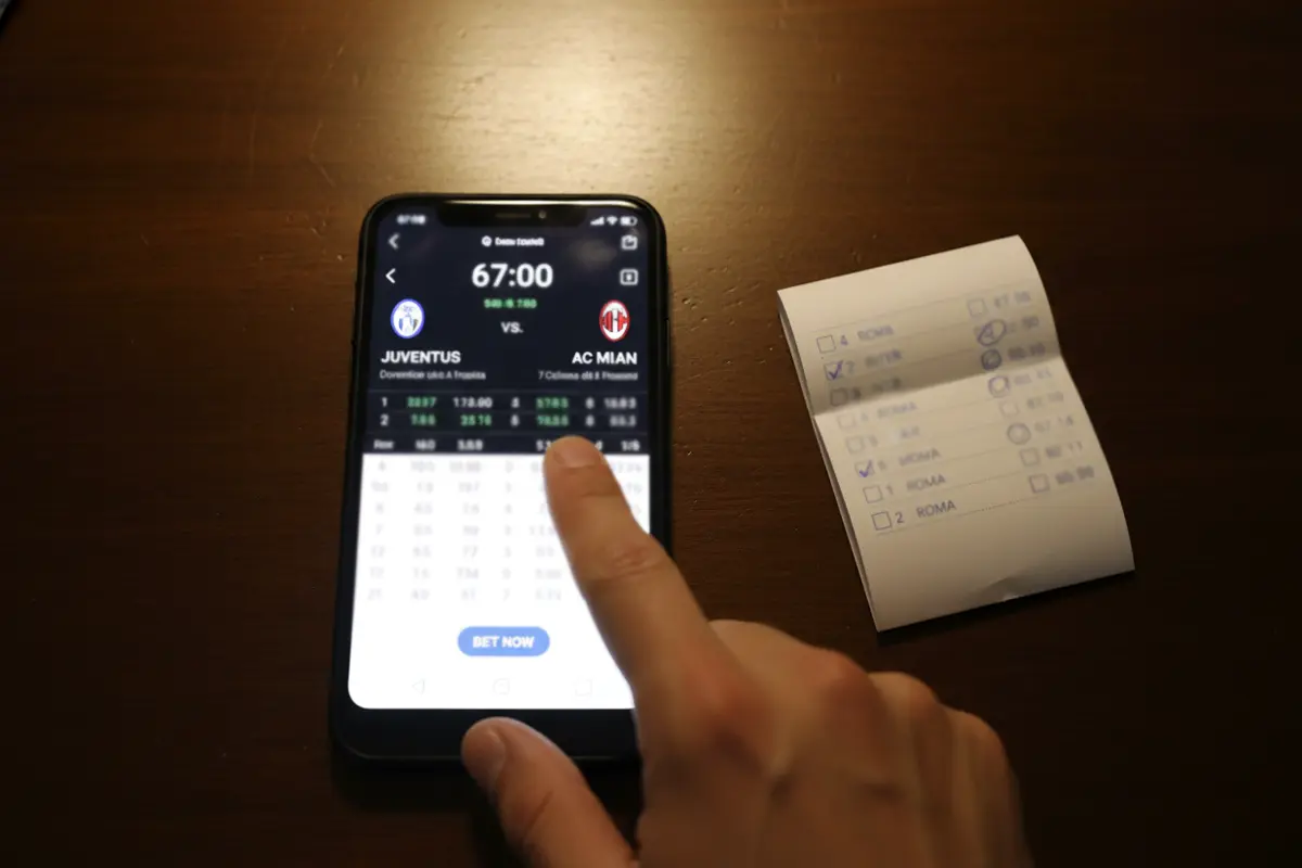 Smartphone con quote live di una partita di calcio in corso accanto a una schedina sistema su un tavolo